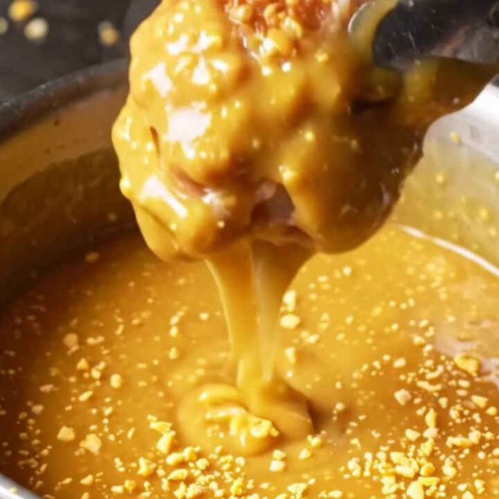 A close-up shot of crispy pretzel-crusted chicken wings drizzled with glossy honey mustard.