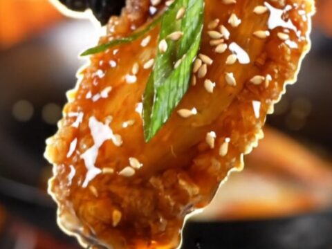 Crispy General Tso's chicken wings coated in a glossy dark glaze and topped with sesame seeds.