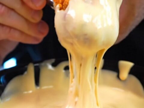 A close-up shot of a vibrant orange Doritos crusted chicken tender being pulled apart to reveal juicy white meat inside.
