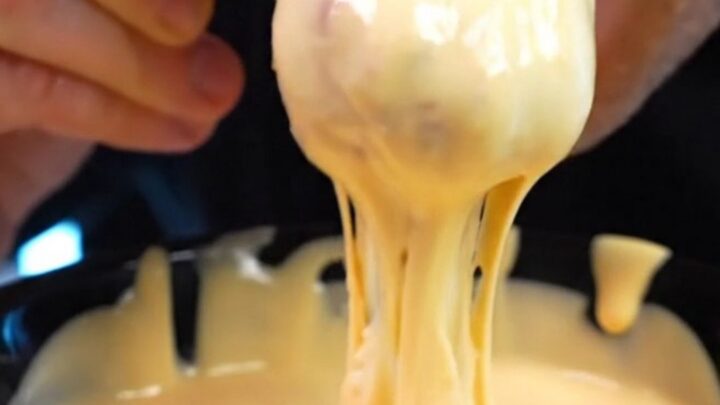 A close-up shot of a vibrant orange Doritos crusted chicken tender being pulled apart to reveal juicy white meat inside.