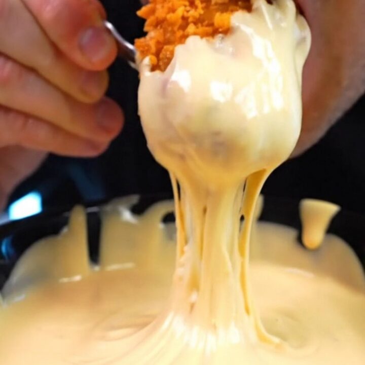 A close-up shot of a vibrant orange Doritos crusted chicken tender being pulled apart to reveal juicy white meat inside.