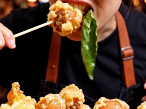 A close-up of golden-brown Taiwanese popcorn chicken with crispy green Thai basil leaves.