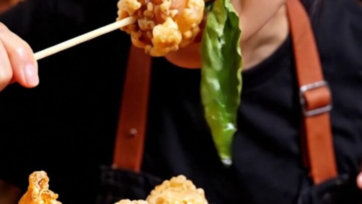 A close-up of golden-brown Taiwanese popcorn chicken with crispy green Thai basil leaves.