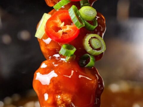Macro close-up of crispy firecracker chicken bites with a glossy red sauce.
