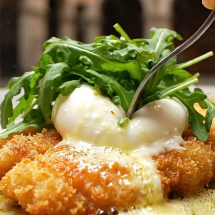 A crispy, golden-brown chicken Milanese cutlet topped with a creamy, torn burrata ball and fresh baby arugula.