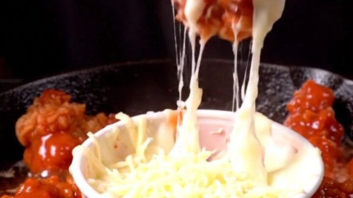 A close-up of a crispy chicken tender being lifted from a skillet, pulling long strands of melted mozzarella cheese.