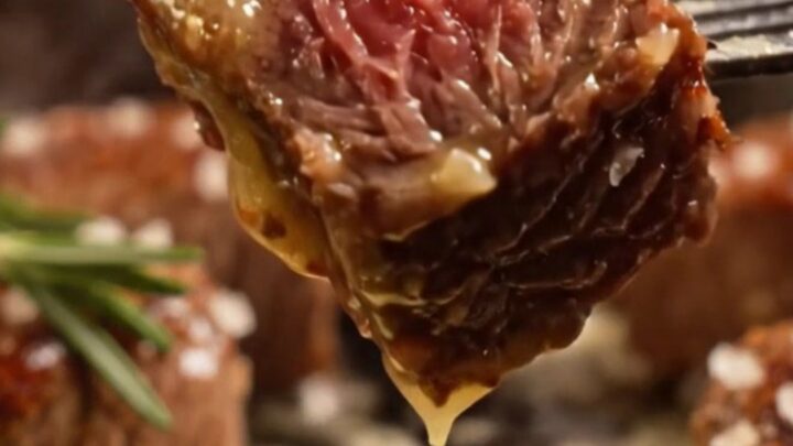 A close-up of seared ribeye steak bites glistening with golden garlic butter in a black cast-iron skillet.
