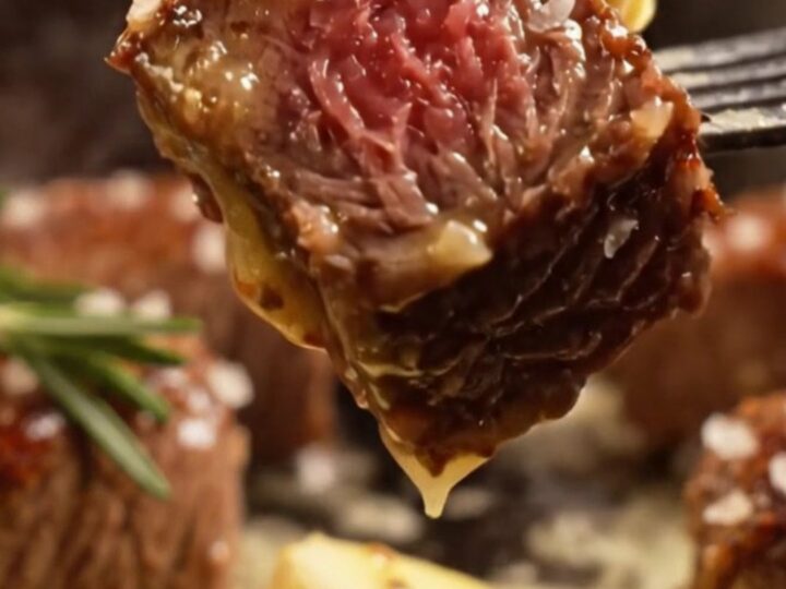 A close-up of seared ribeye steak bites glistening with golden garlic butter in a black cast-iron skillet.