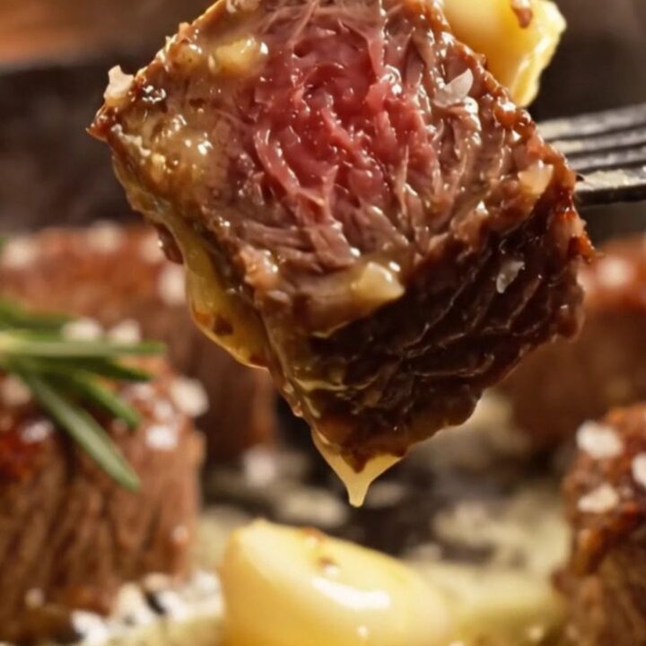 A close-up of seared ribeye steak bites glistening with golden garlic butter in a black cast-iron skillet.