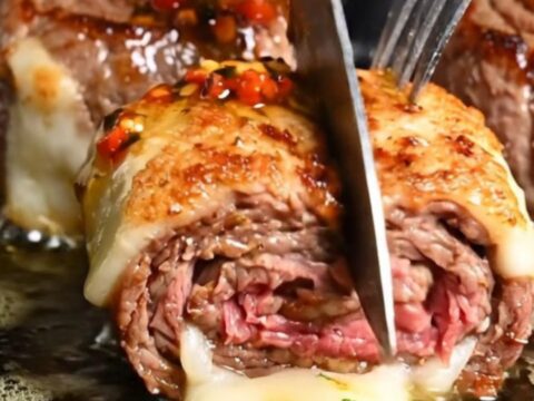 A close-up of a perfectly seared flank steak pinwheel with visible layers of melted provolone and roasted peppers.