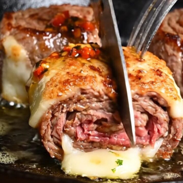 A close-up of a perfectly seared flank steak pinwheel with visible layers of melted provolone and roasted peppers.
