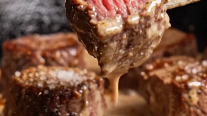 A close-up of tender filet mignon bites with a cracked black pepper crust, drizzled in a rich, creamy cognac sauce.