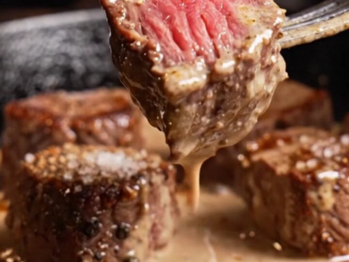 A close-up of tender filet mignon bites with a cracked black pepper crust, drizzled in a rich, creamy cognac sauce.
