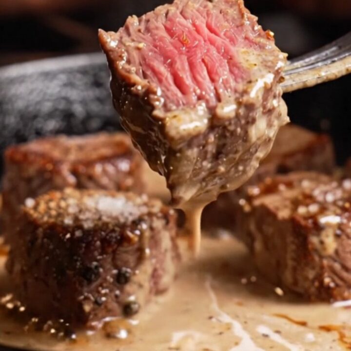 A close-up of tender filet mignon bites with a cracked black pepper crust, drizzled in a rich, creamy cognac sauce.