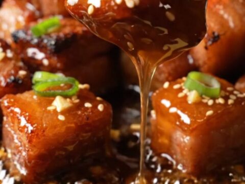 A close-up of honey garlic pork belly burnt ends on a plate, glistening with a sticky glaze and garnished with sesame seeds.