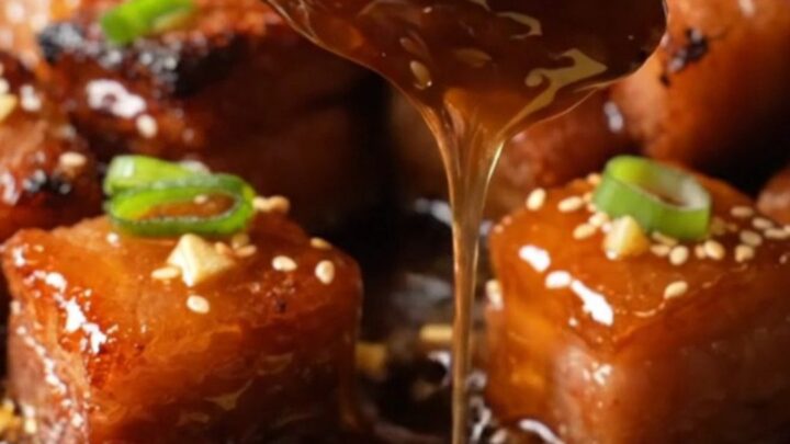 A close-up of honey garlic pork belly burnt ends on a plate, glistening with a sticky glaze and garnished with sesame seeds.