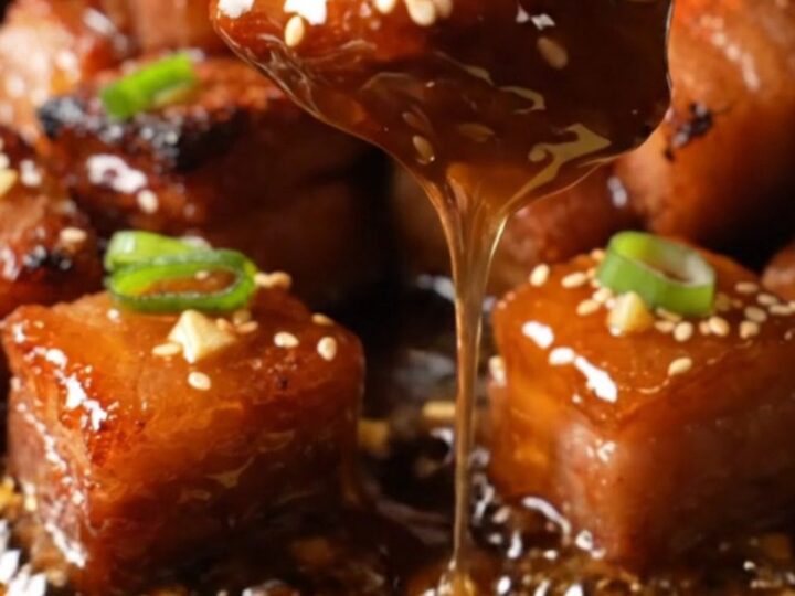 A close-up of honey garlic pork belly burnt ends on a plate, glistening with a sticky glaze and garnished with sesame seeds.