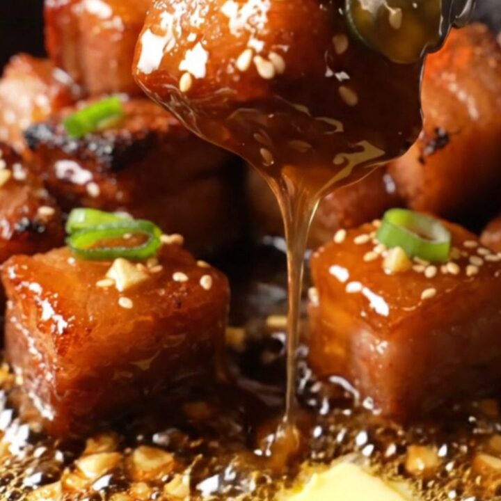 A close-up of honey garlic pork belly burnt ends on a plate, glistening with a sticky glaze and garnished with sesame seeds.