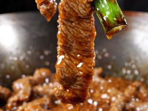 A close-up of crispy Mongolian beef strips with a dark glossy glaze and vibrant green scallions.