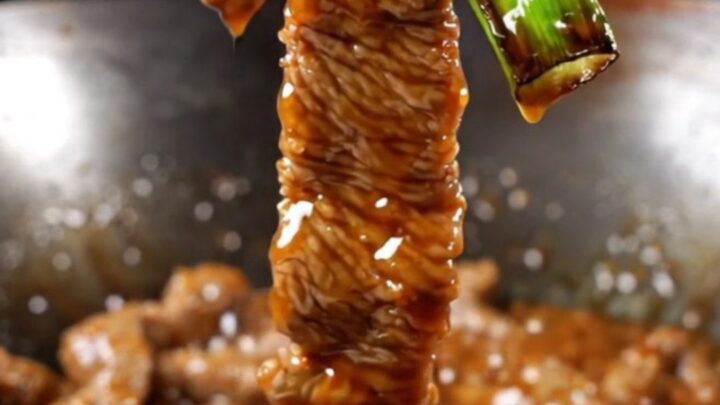 A close-up of crispy Mongolian beef strips with a dark glossy glaze and vibrant green scallions.