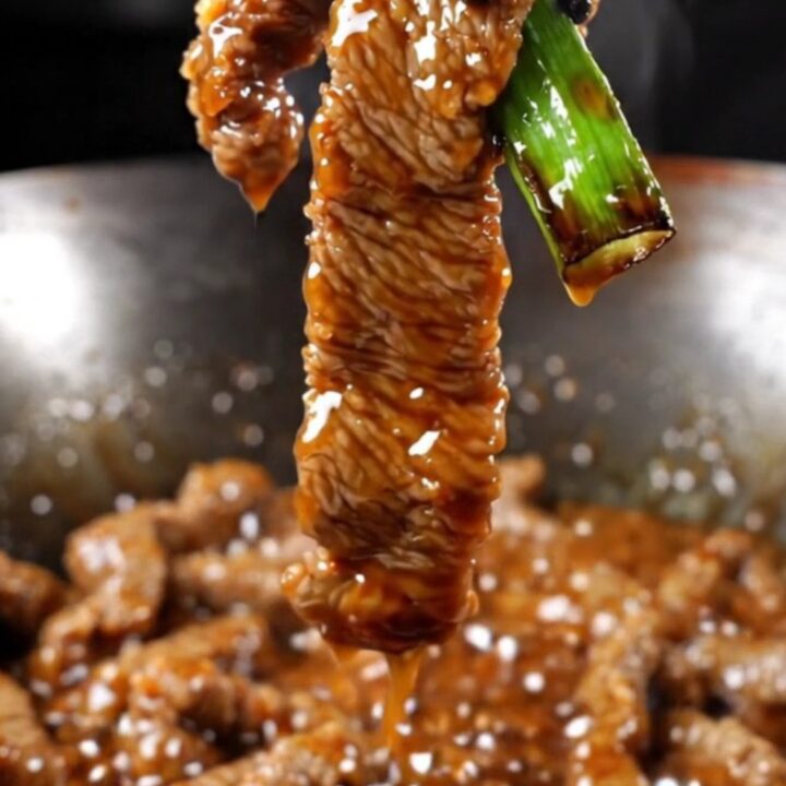 A close-up of crispy Mongolian beef strips with a dark glossy glaze and vibrant green scallions.