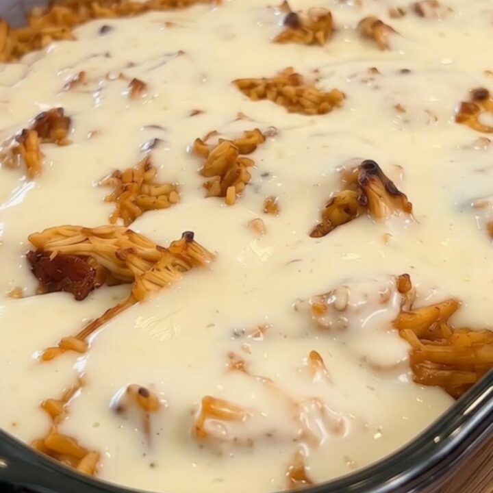 A glass baking dish filled with golden seasoned rice and shredded chicken, smothered in a thick layer of melted white queso.