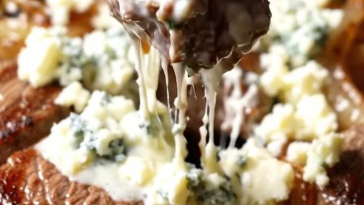 Close-up of seared steak bites in a cast-iron skillet topped with melting Gorgonzola and caramelized onions.