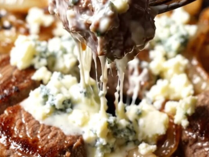 Close-up of seared steak bites in a cast-iron skillet topped with melting Gorgonzola and caramelized onions.