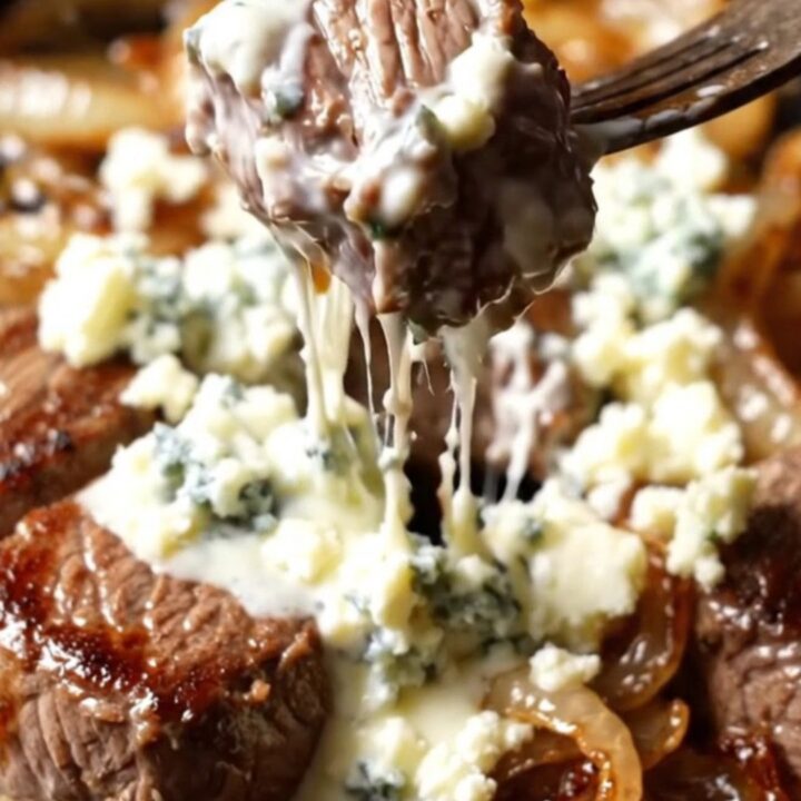 Close-up of seared steak bites in a cast-iron skillet topped with melting Gorgonzola and caramelized onions.