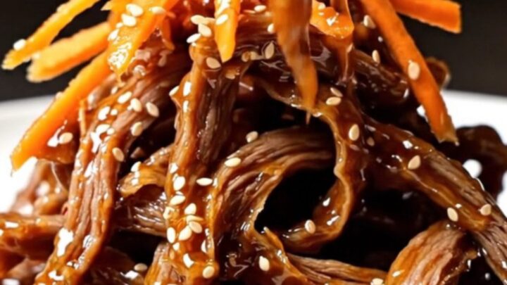 A close-up of crispy, glazed beef matchsticks piled high on a plate, garnished with vibrant orange carrots and sesame seeds.