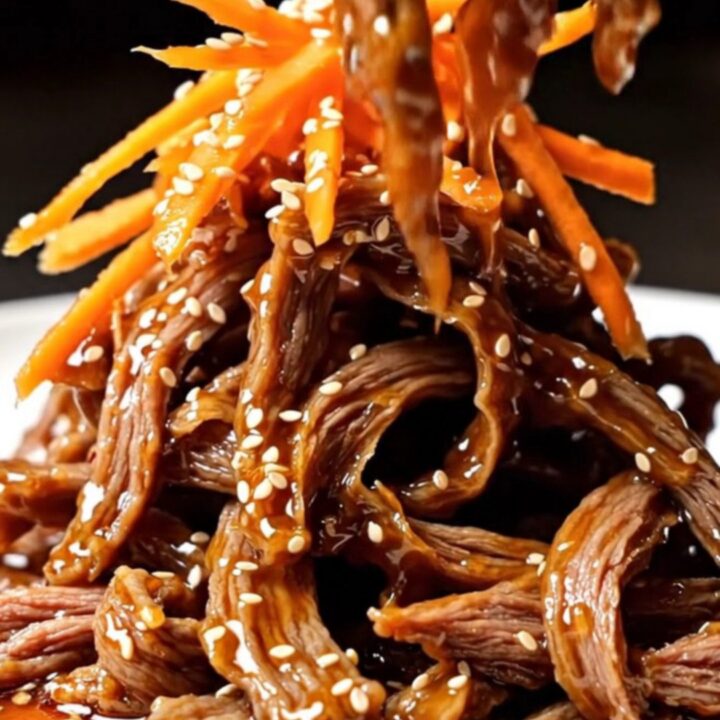 A close-up of crispy, glazed beef matchsticks piled high on a plate, garnished with vibrant orange carrots and sesame seeds.
