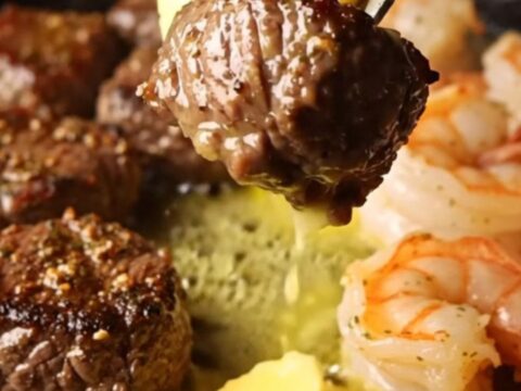 A cast-iron skillet filled with seared steak bites and jumbo shrimp in a golden lemon herb butter sauce.
