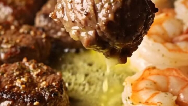 A cast-iron skillet filled with seared steak bites and jumbo shrimp in a golden lemon herb butter sauce.
