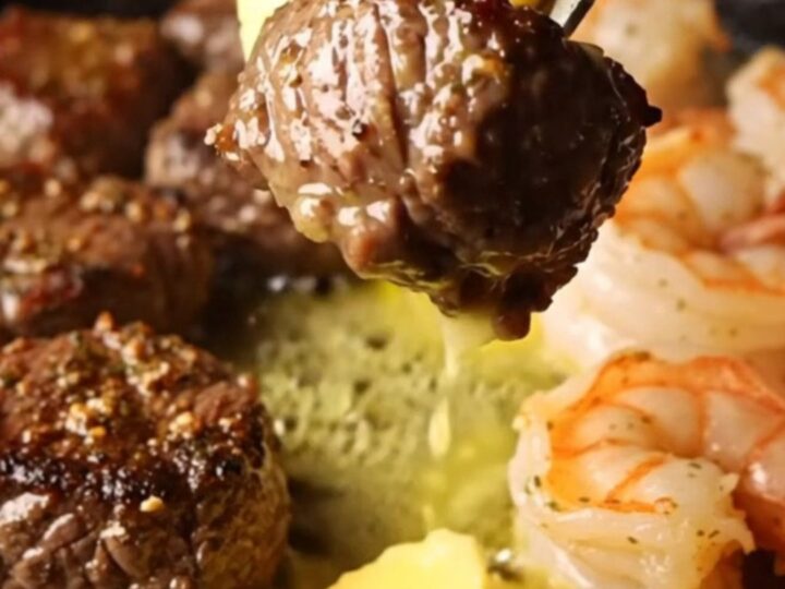 A cast-iron skillet filled with seared steak bites and jumbo shrimp in a golden lemon herb butter sauce.