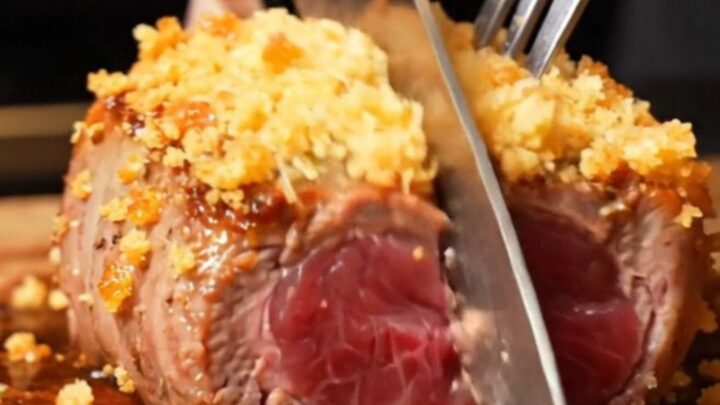 A close-up of golden garlic parmesan crusted lamb loin chops in a cast-iron skillet with ruby-pink centers.
