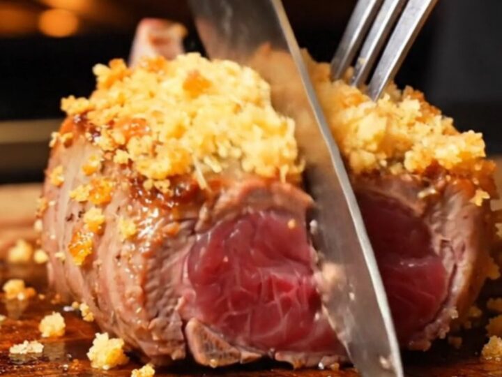 A close-up of golden garlic parmesan crusted lamb loin chops in a cast-iron skillet with ruby-pink centers.