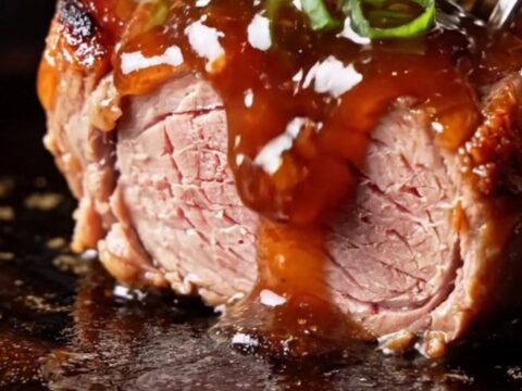 A close-up view of sticky, caramelized Char Siu pork medallions with a deep ruby-red glaze and charred edges.