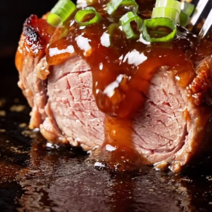 A close-up view of sticky, caramelized Char Siu pork medallions with a deep ruby-red glaze and charred edges.