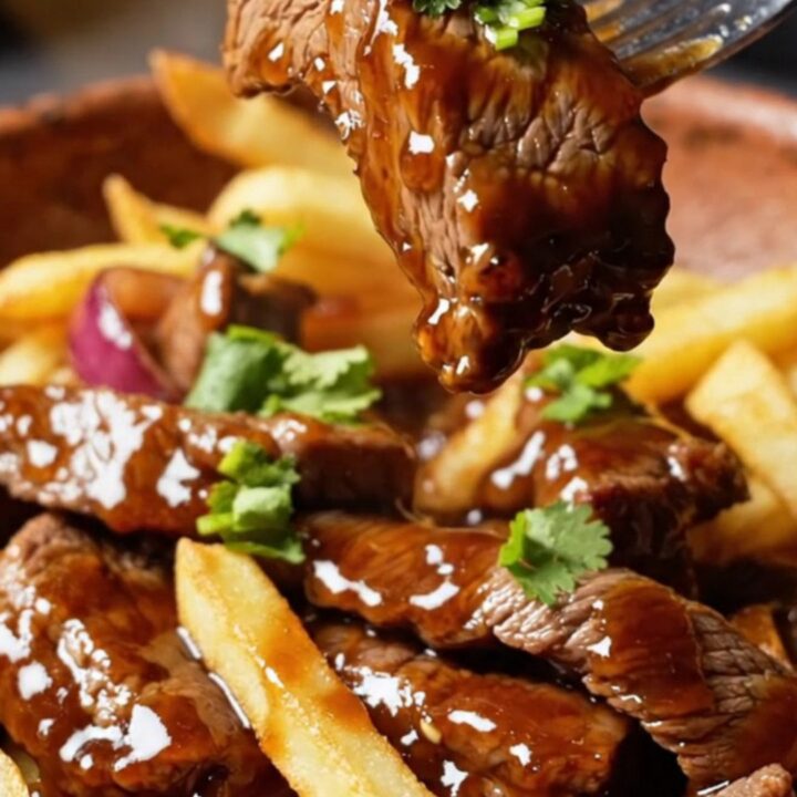 A vibrant plate of Peruvian lomo saltado featuring charred beef strips, blistered onions, and golden fries.