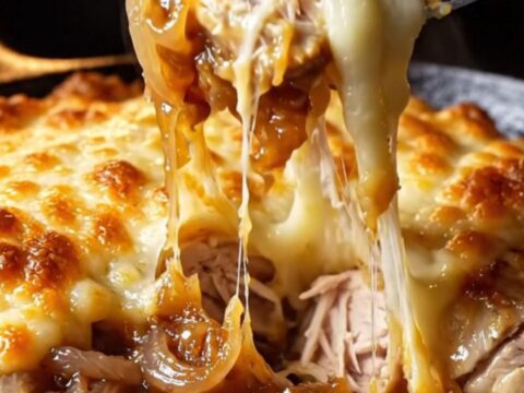 A golden-brown chicken breast in a cast-iron skillet topped with melted, bubbling Gruyère cheese and jammy onions.