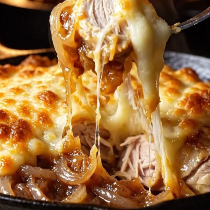 A golden-brown chicken breast in a cast-iron skillet topped with melted, bubbling Gruyère cheese and jammy onions.