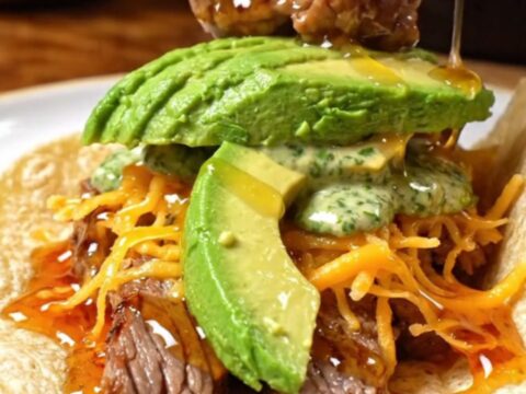 A close-up shot of a chipotle honey flank steak taco with a golden crispy Oaxaca cheese crust.