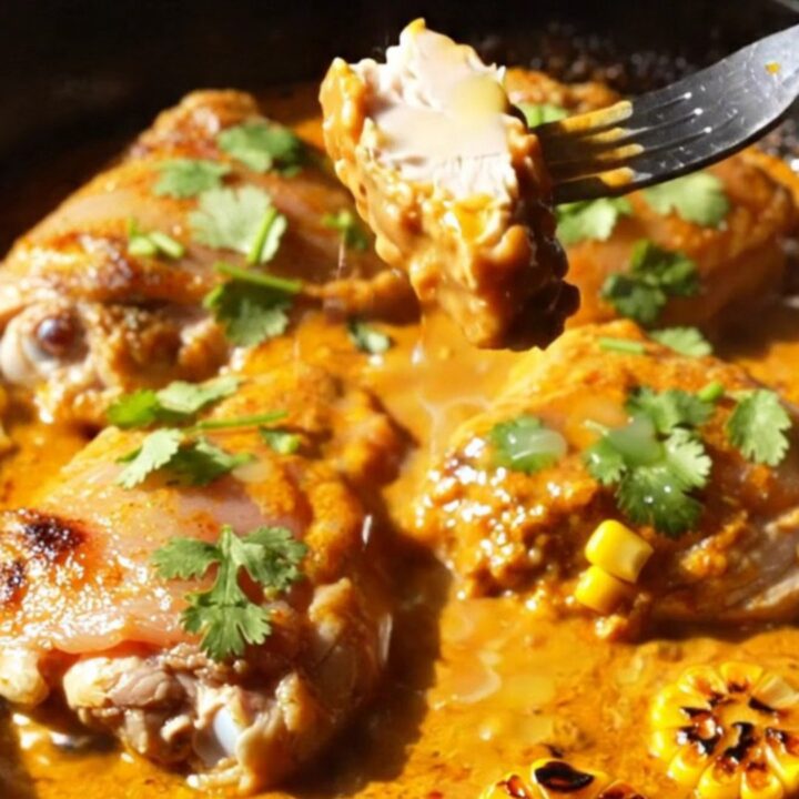 A cast iron skillet filled with crispy golden-brown chicken thighs, charred corn