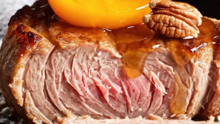 A close-up of thick-cut pork chops topped with caramelized peach wedges and toasted pecans in a cast-iron skillet.