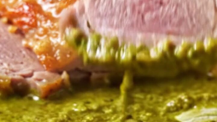 A perfectly seared duck breast with crispy golden skin resting in a pool of vibrant green Thai curry sauce.