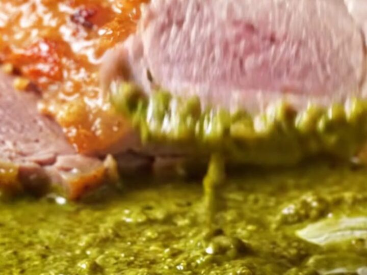 A perfectly seared duck breast with crispy golden skin resting in a pool of vibrant green Thai curry sauce.