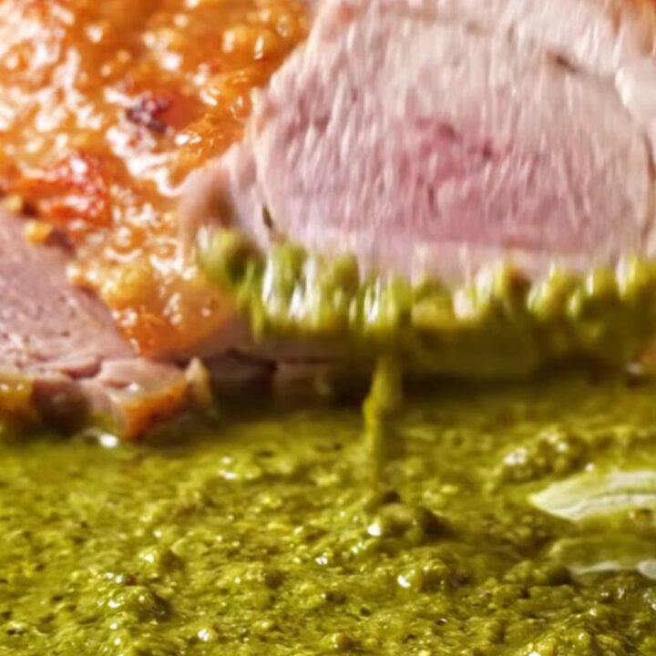 A perfectly seared duck breast with crispy golden skin resting in a pool of vibrant green Thai curry sauce.