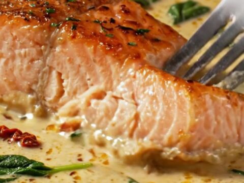 A close-up of crispy skin salmon fillets served in a creamy sun-dried tomato and spinach sauce.