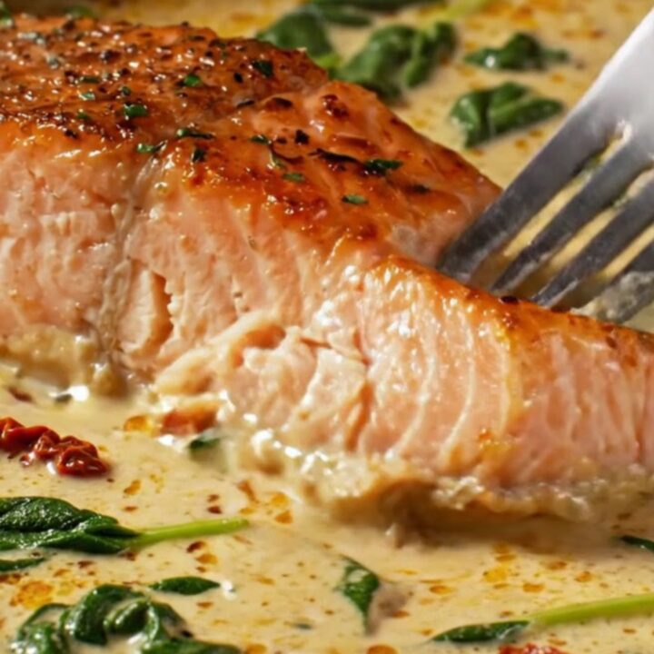 A close-up of crispy skin salmon fillets served in a creamy sun-dried tomato and spinach sauce.