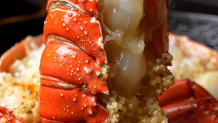A close-up of a perfectly cooked lobster tail, glistening with garlic butter and fresh herbs.
